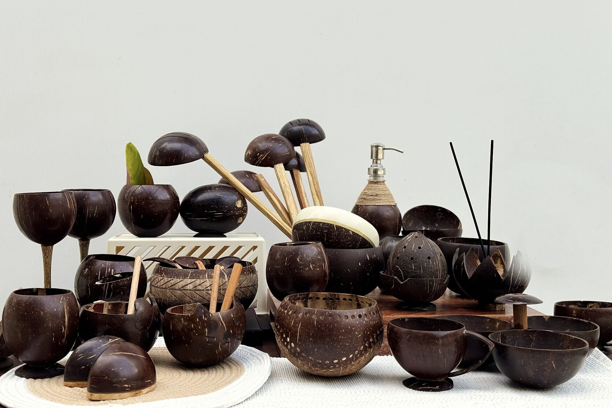 The Thenga Story range laid out on a table: goblets, breakfast bowls, cups, lamps, a soap dispenser and an incense holder, every one turned from a coconut shell.