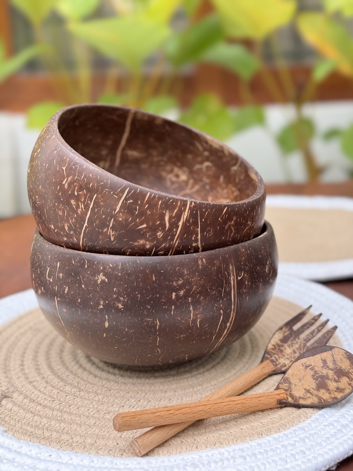 Two polished coconut shell bowls stacked with carved cutlery