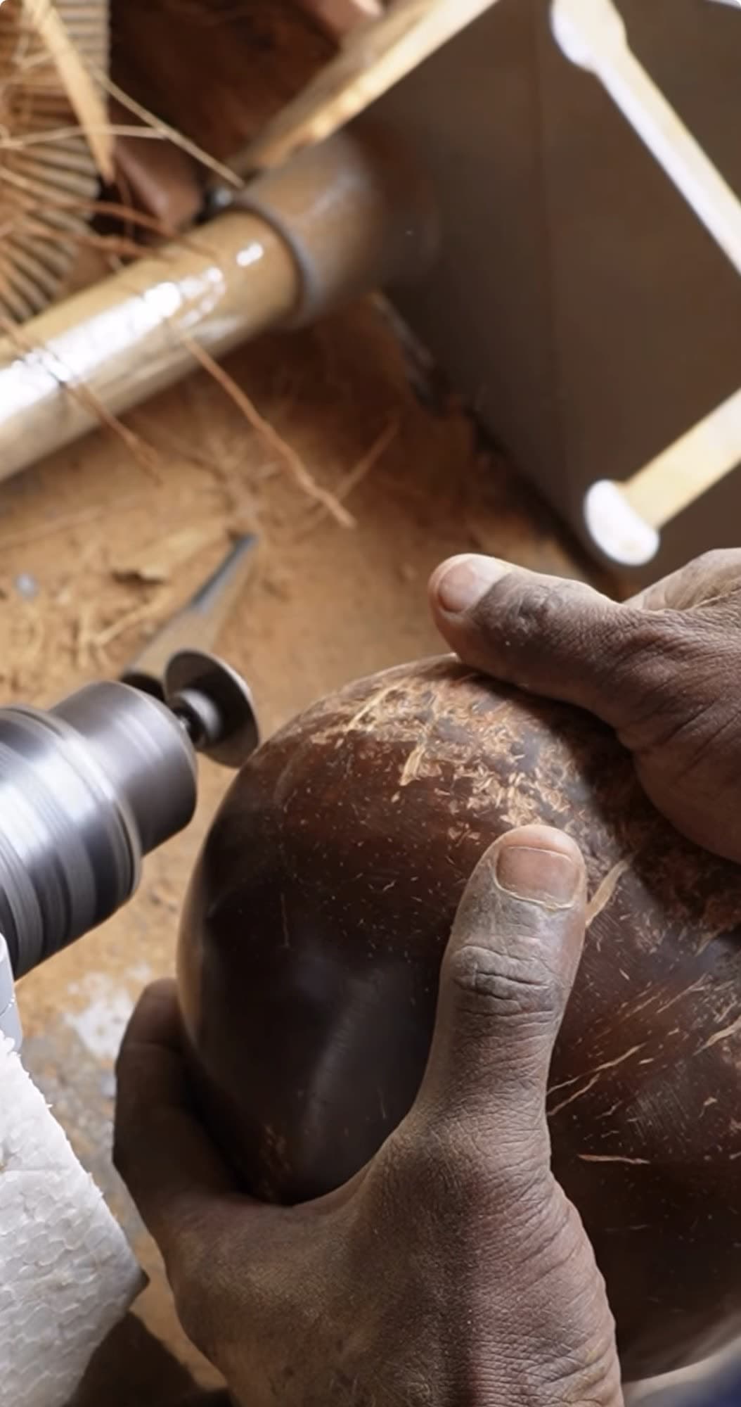 An artisan's hands shaping a coconut shell against a sanding wheel